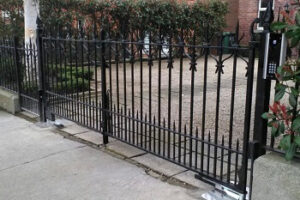 Straight across black gate with matching pedestrian gate and railings. Underground FAAC automation visible, Intercom with keypad attached to pier. Cobblestone driveway