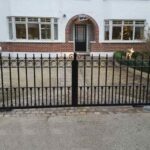 Black steel gate set between two short redbrick pillars.